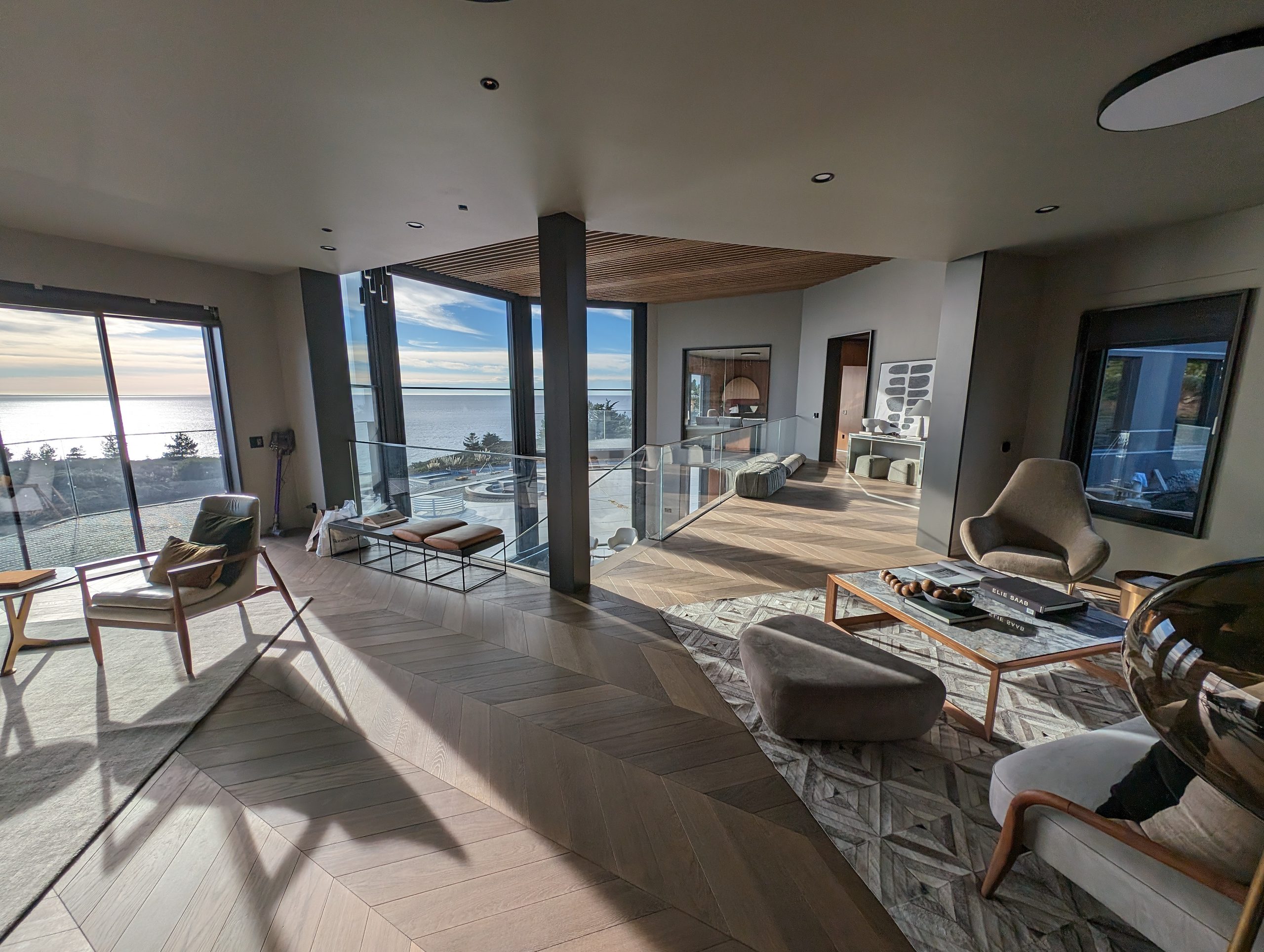 Living room opening through full-height glass to the Pacific, with slatted wood ceiling