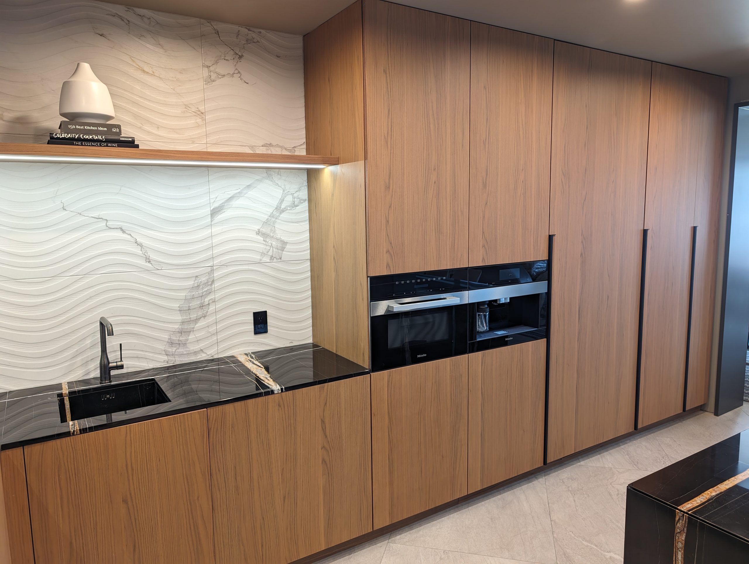Prep kitchen with full-height walnut units, integrated ovens, and a relief-cut marble backsplash