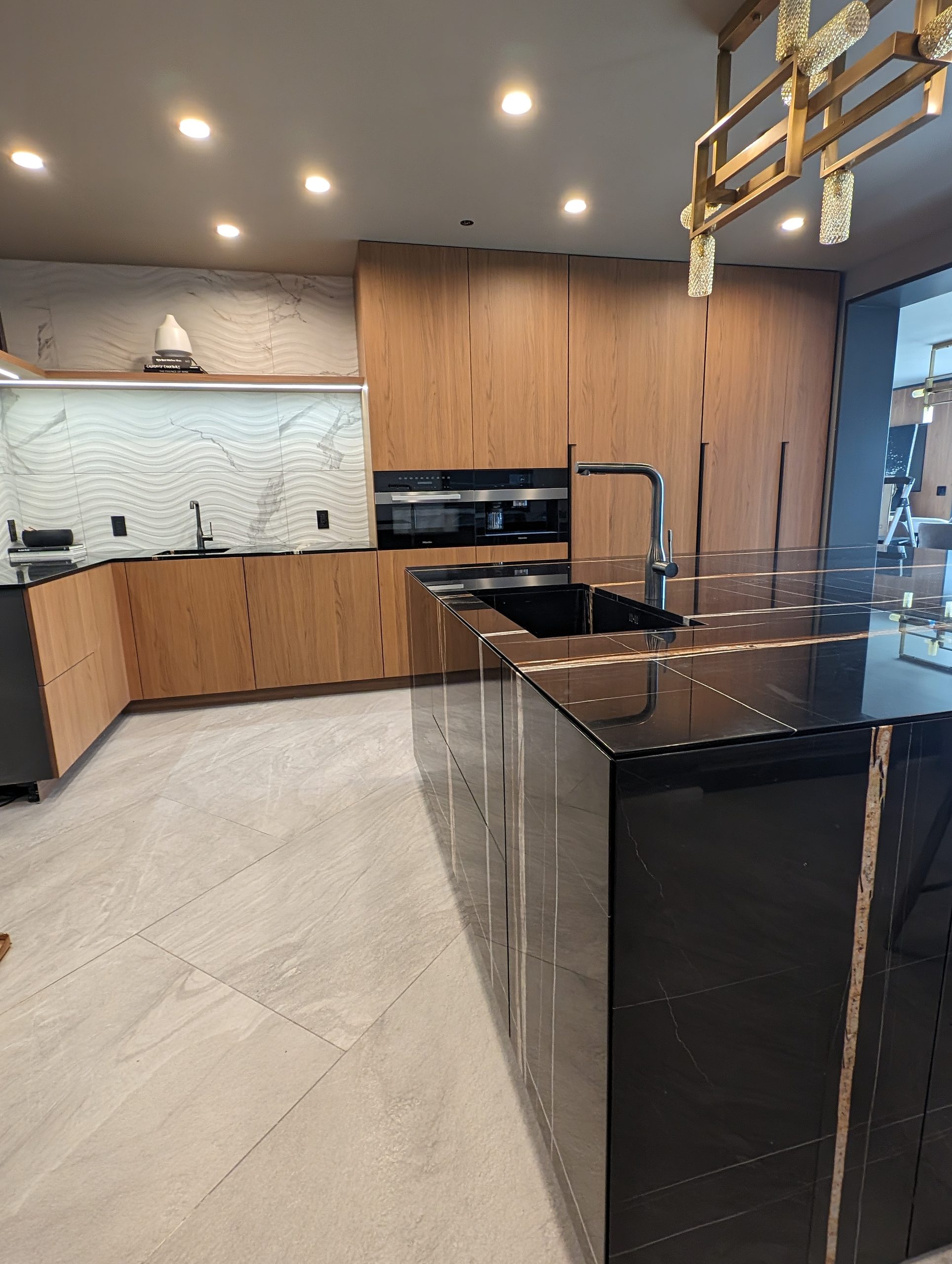Main kitchen with walnut fronts and a black marble island under a brass chandelier
