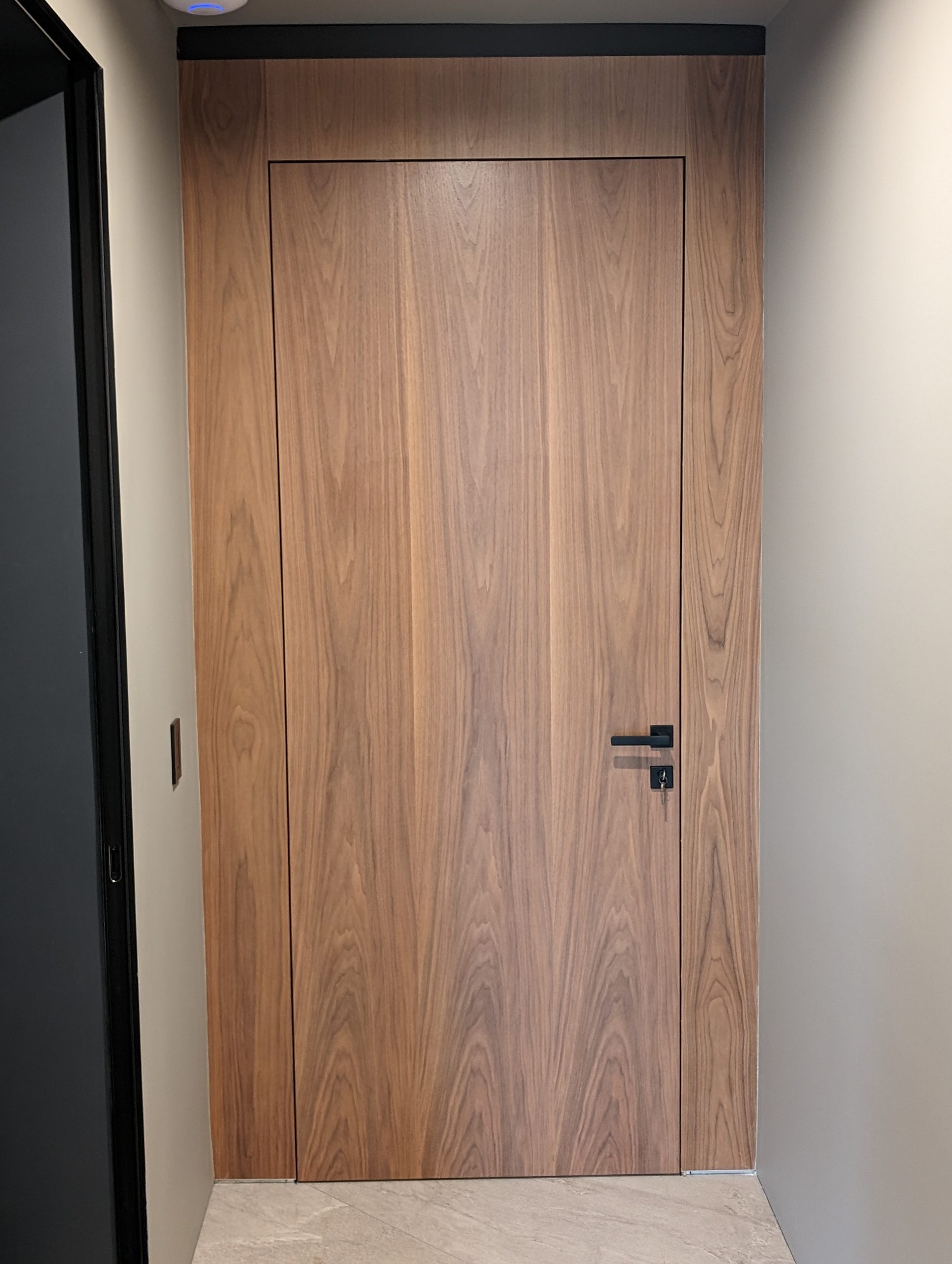 Flush walnut door with a black lever, hung in a matching walnut jamb