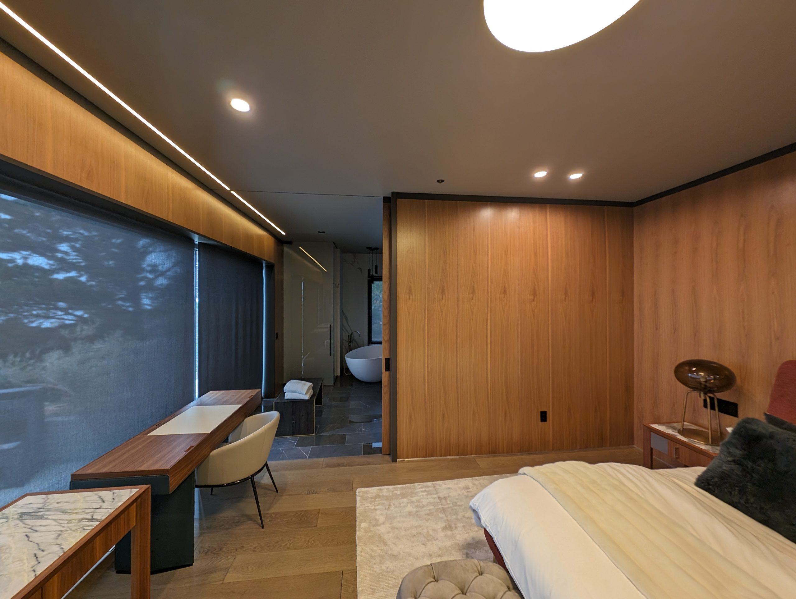 Bedroom with continuous walnut wall, integrated lighting, and the bath beyond