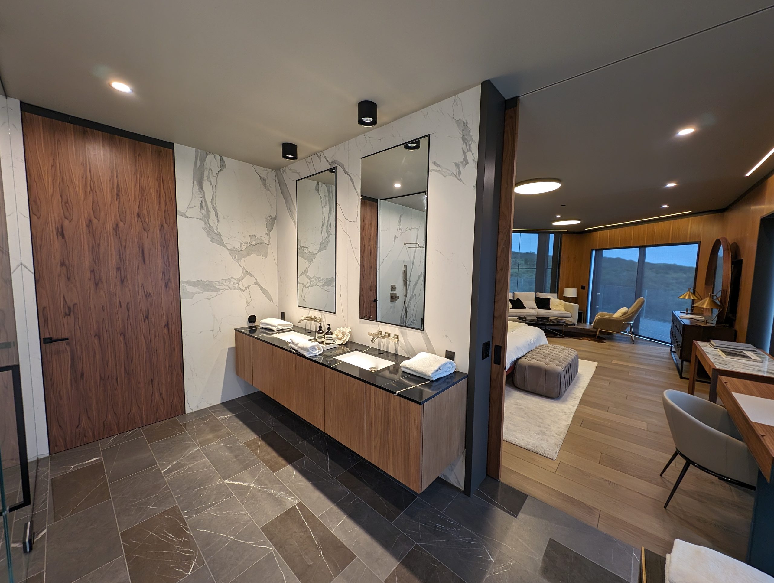 Primary bath with a floating walnut double vanity against full-height marble