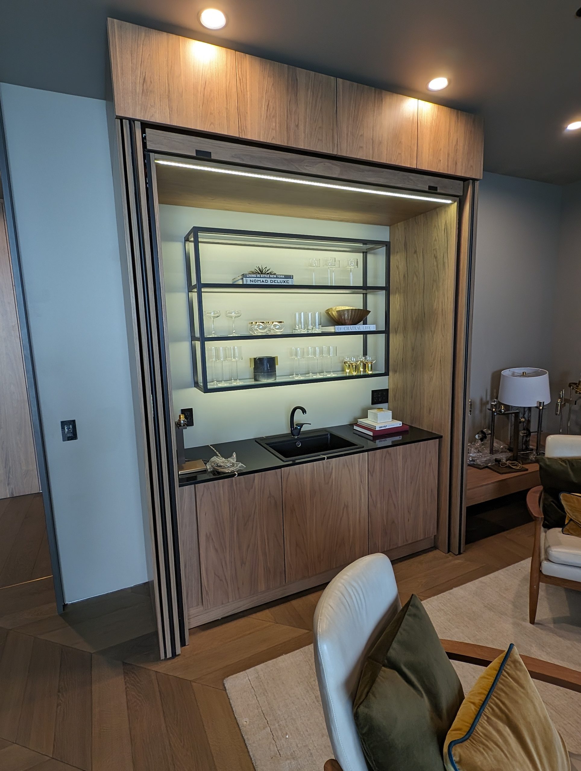 Bar cabinet with retracting pocket fronts, lit glass shelving, and an integrated sink