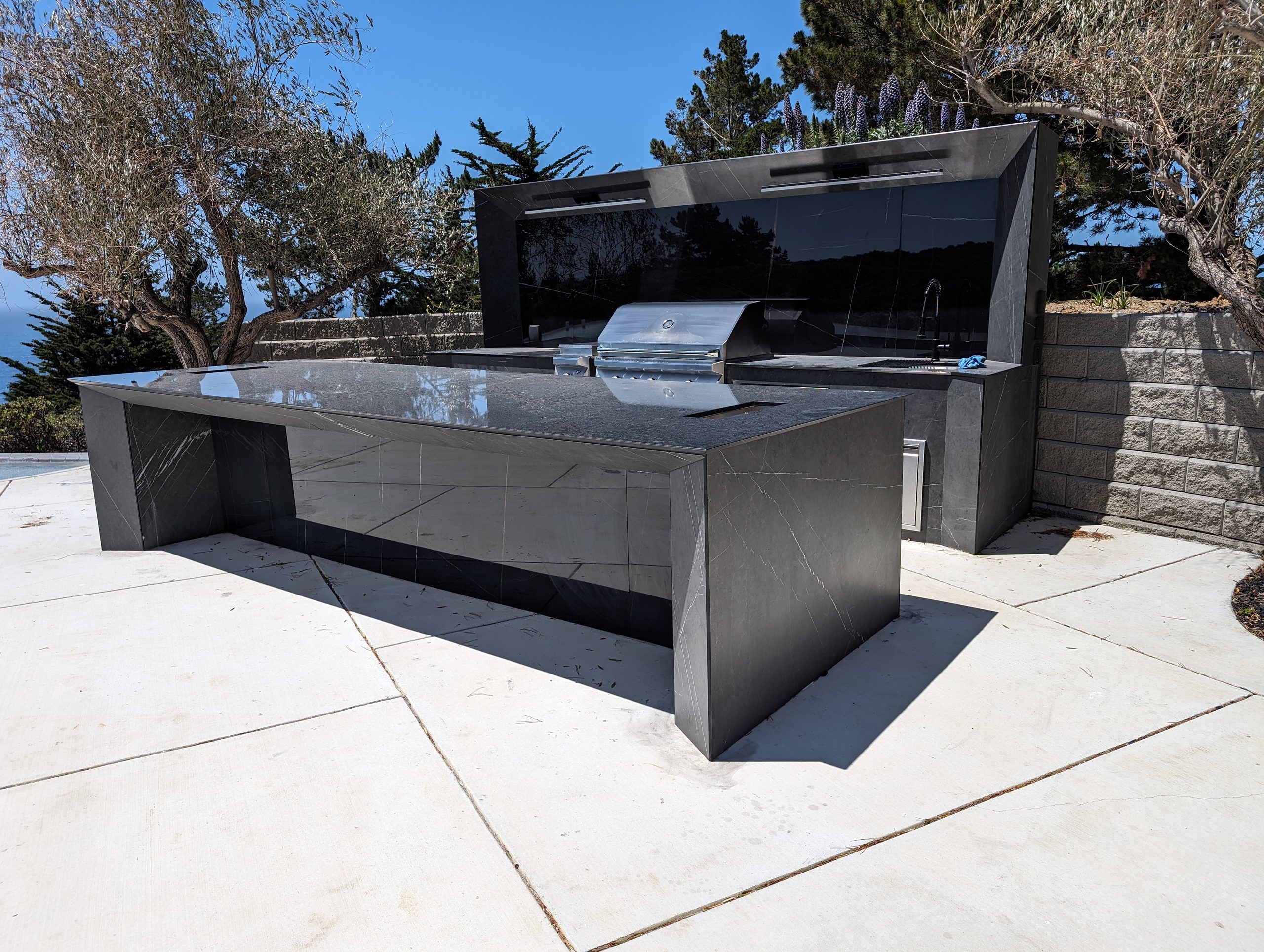 Dark stone outdoor island with grill, ventilation hood, and mitred edges