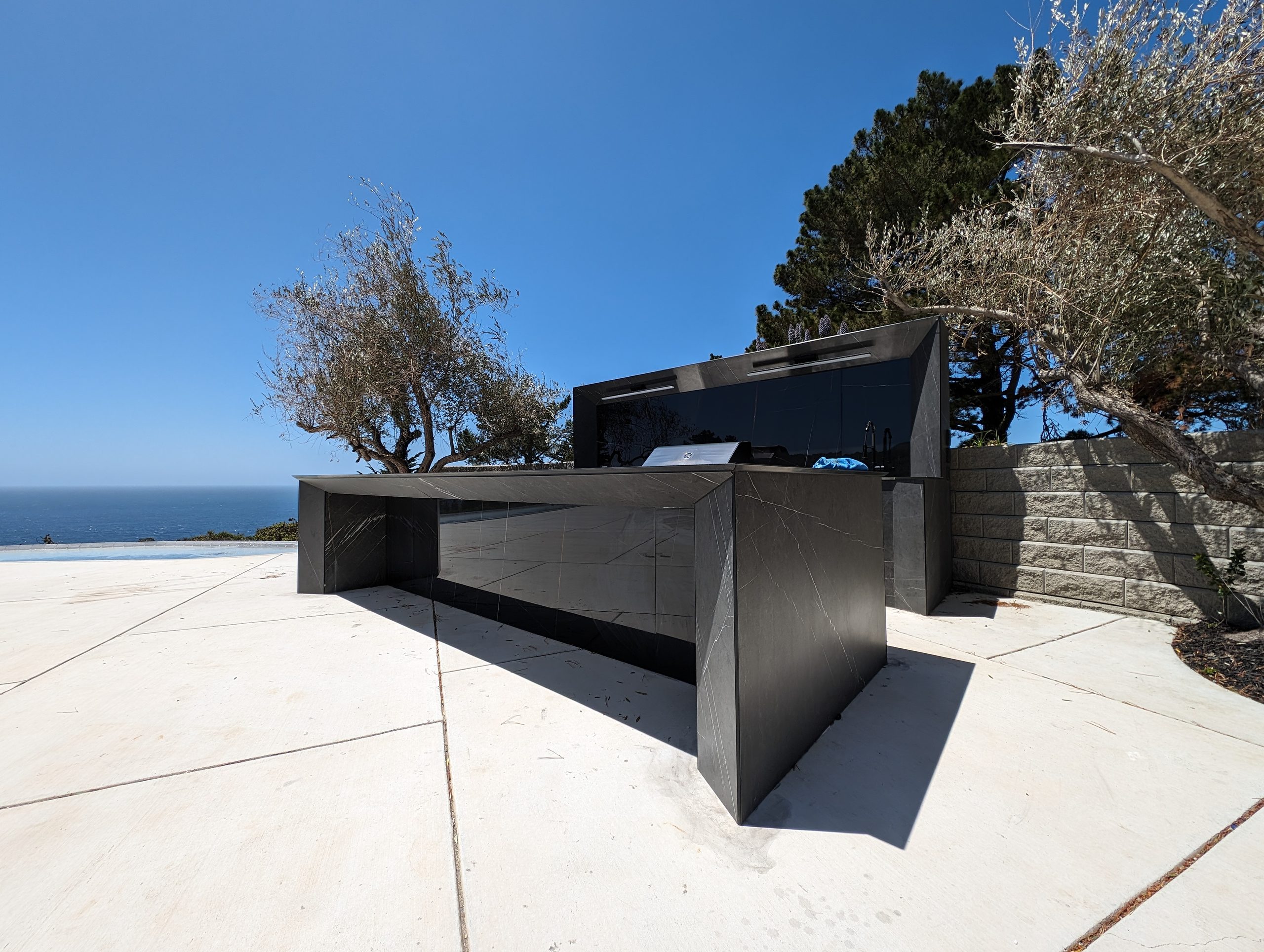 The terrace kitchen seen from the pool deck, olive trees and the Pacific behind
