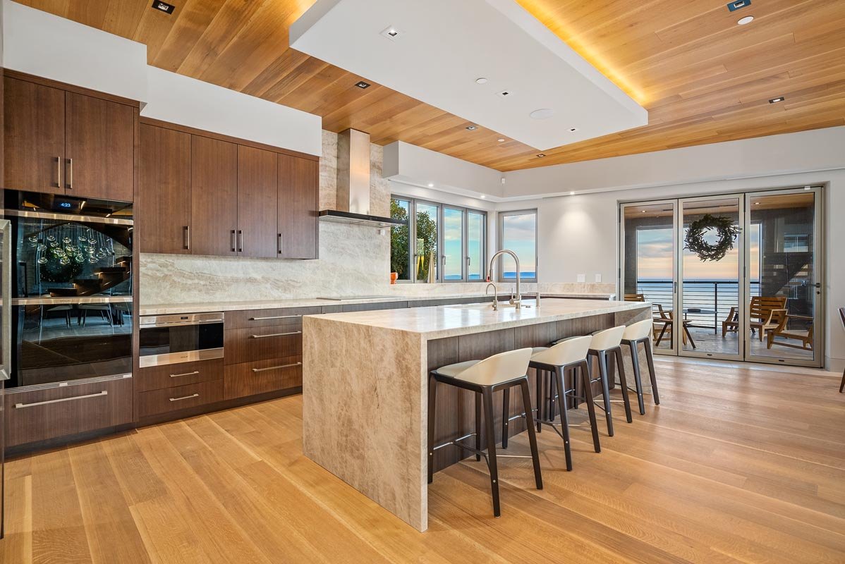 Kitchen in walnut with quartzite waterfall island, glass doors open to the water