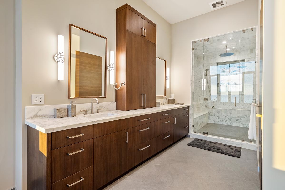 Primary bath — floating walnut double vanity with lit mirrors and glass shower